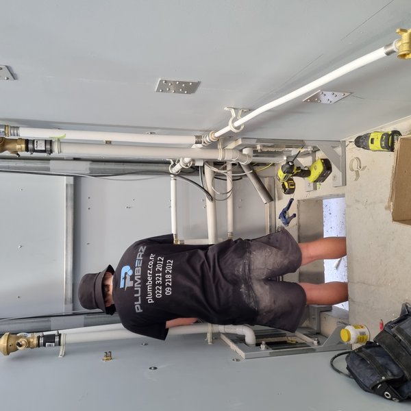 Plumberz plumber working on pipework in a wall chase in West Auckland