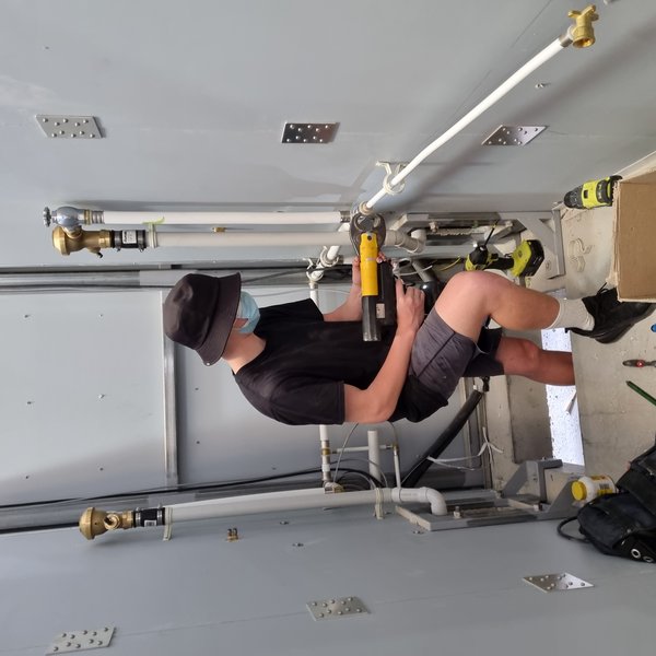 Plumberz plumber cutting PVC pipe with a power cutter during a West Auckland install